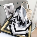 Détail d'un foulard en soie géométrique noué à un sac à main beige avec décor minimaliste - Gris