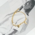 Elegante bracciale in titanio dorato con perla, ciondolo a croce e charm LOVE su sfondo moda - Oro