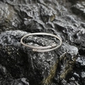 Brazalete rígido trenzado de acero de titanio pulido sobre superficie de piedra oscura - Color Acero