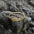 Elegante brazalete dorado de acero de titanio con diseño trenzado sobre fondo de roca - Estilo Dorado