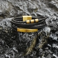 Bracciale multistrato in pelle intrecciata nera con chiusura magnetica dorata su roccia scura - Oro