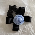 Detail of black satin bow scrunchie featuring a light blue silk rose on white paper - Blue