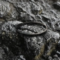 Minimalist black oval titanium steel bangle with polished finish on dark rock surface - Shiny Black (Large)