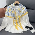 Detail van witte chiffon blouse met een geel-blauwe bloemensjaal geknoopt bij de halslijn - Geel