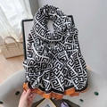 Detail of a geometric monochrome scarf with a vibrant orange border on a grey chair - Chocolate