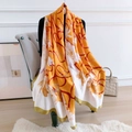 Detail eines Seidenschals mit gelbem Kettenprint elegant auf einem Ständer drapiert - Orange