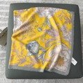 Detail of yellow floral silk scarf with frayed edges and brand tag on a soft stool - 130x130cm / Yellow