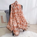 Détail d'une écharpe en soie élégante avec motif floral orange et bordure marron foncé - Café Clair