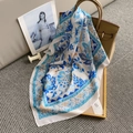 Detail of floral patterns on ivory satin scarf next to a brown bag on grey carpet - Blue