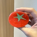 Detail view of red marbled acetate hair clip with teal starfish pattern held in hand - Tomato