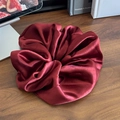 Elegante elastico scrunchie in raso rosso vino su un tavolo di legno scuro - Elastico per capelli