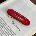 Fermaglio ovale rosso vintage con strass colorati su sfondo di un libro retrò - Rosso