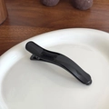Glossy black wave shaped hair clip with jelly texture on white ceramic plate - Black