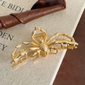Golden spider-shaped metal hair claw clip with vintage alloy finish on retro book - Gold Spider Claw