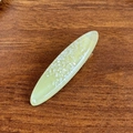 Ovale hellgrüne Acetat-Haarklammer mit schimmernden Pailletten auf dunklem Holzgrund - 5.9cm / Grün