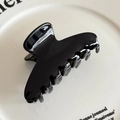 Glossy black acetate hair claw clip with golden logo accent on white ceramic tray - Black No Label