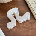 Iridescent white acetate wave-shaped hair claw clip on dark wooden surface - Pearlescent Light Pink (Gold Label)