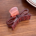 Elegant dark red translucent bow hair claw clip in acetate finish on wooden background - Caramel color