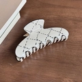Creamy white hair claw clip with black argyle pattern and crystals on wood surface - Cream