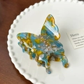 Macro shot of butterfly-shaped acetate hair claw with sparkling crystals on a porcelain plate - Teal / 8.3cm