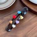 Fermaglio per capelli nero traforato con sei cuori colorati su sfondo di legno - Marrone