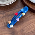 Blue Maillard hair clip with colorful 3D heart charms on a rustic wooden background - Blue