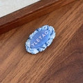 Barrette à cheveux bleu marbré avec lettrage YLETAO rose sur surface boisée - Nuage Bleu