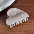 Khaki heart-shaped hair claw with white doodle patterns on a dark wooden background - Brown Heart Shape