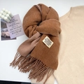 Close-up of brown cashmere-feel scarf detail featuring fringe and brand logo label - Orange Brown