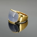 Goldener Siegelring mit ovalem blauem Katzenaugenstein auf dunkler Spiegelfläche - Goldbasis Lila Stein