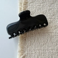 Primer plano de una pinza para el pelo negra brillante con dientes fuertes sobre un tapiz - Negro