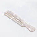 Macro shot of pearlized marble texture on a wide-tooth acetate hair comb with smooth finish - White