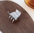 Pinza pequeña de metal plateado brillante para coleta alta sobre superficie de madera - Plateado
