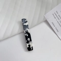 Detail of a rectangular acetate hair clip with black and white marble pattern on white fabric - One Size