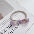 Detail of a marble-textured bow hair tie with a gold handmade logo on a magazine - Floral Purple