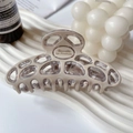 Macro detail of French acetate hair claw with hollow mesh design and engraved text - Grey/White