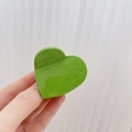 Pinza de pelo brillante en forma de corazón verde intenso sostenida ante pared - Verde