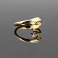 Polished gold embrace ring with hand-shaped hug design on a reflective grey surface - Gold