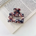 Square acetate claw clip with dark red and beige tortoiseshell pattern on a vintage book - Brown