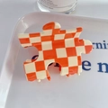 Puzzle shaped acetate hair claw clip with orange checkerboard pattern on white tray - Orange