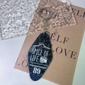 Macro detail of dark blue marble acrylic hotel key tag with white text and silver metal ring - Gold Accessories / Black