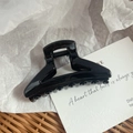 Close-up of a glossy black hair claw clip with rounded teeth and strong metal spring detail - Black