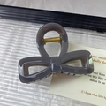 Close-up of a dark grey bow-shaped hair claw clip with a strong golden metal spring - Gray