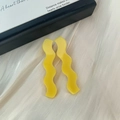 Vue détaillée de pinces à cheveux ondulées jaunes en acétate sur un tissu en soie élégant - Jaune