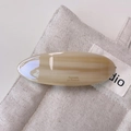 Macro detail of amber acetate barrette hair clip with glossy finish on textured fabric - Beige