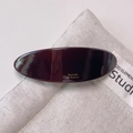 Close-up of a burgundy acetate hair barrette with gold lettering on a canvas bag background - Chocolate