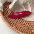 Glossy burgundy oval acetate hair clip with gold lettering on a woven tray - Red