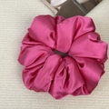Close-up of a large magenta satin scrunchie with soft folds on a white knit background - Rose Red