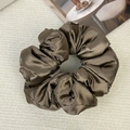 Detail of a large satin scrunchie in deep bronze with smooth texture on a beige background - Brown