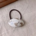 Detailed macro shot of oval marble pattern acetate hair tie with Sanshine brand logo - White Coffee